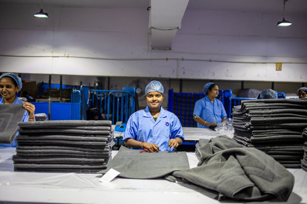 Smiling workers in a textile factory sorting large fabric stacks efficiently.
