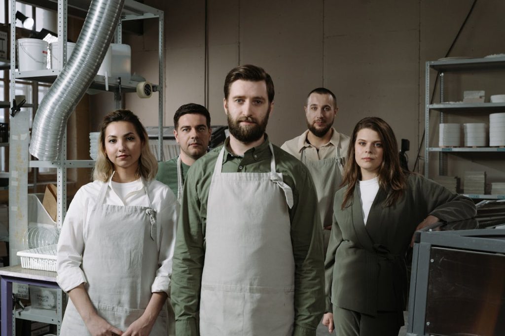 A diverse group of artisans standing together in a pottery studio, dressed in aprons.